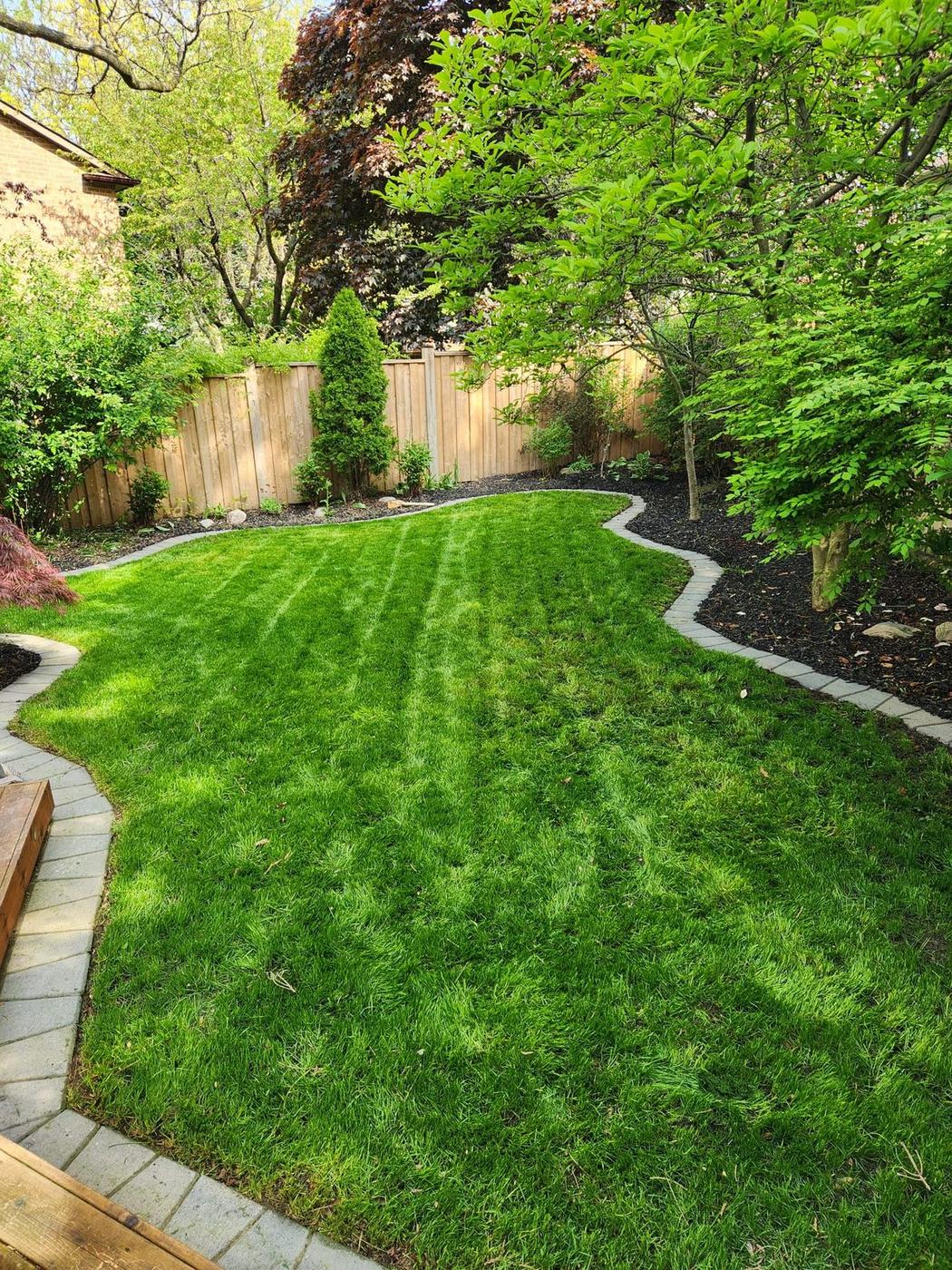 Mowed, striped lawn with curved stone edging and mulched beds