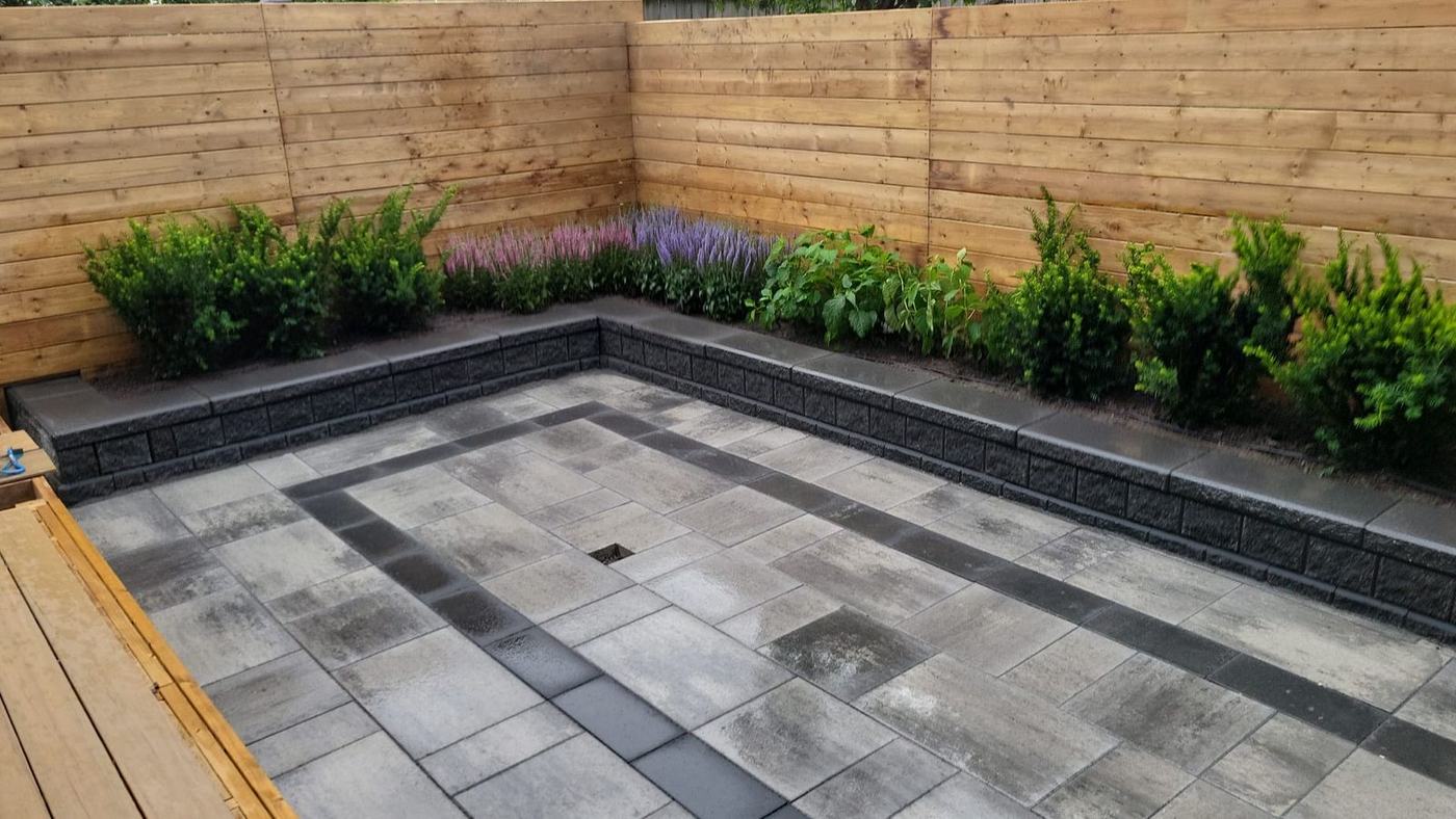 Paver patio with a dark inlay border, raised planter wall and cedar fence