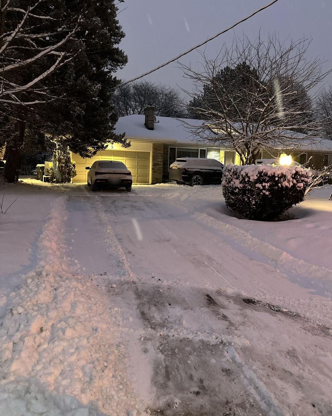 Residential driveway plowed at dusk during a snowfall