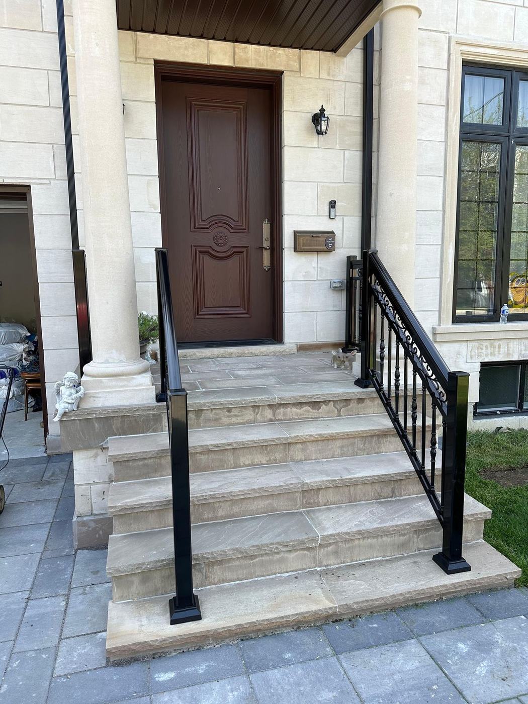 Stone front entrance steps with black railings and a paver landing